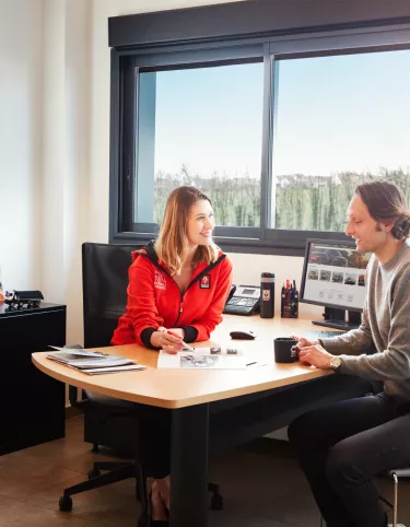 A customer and a saleswoman discuss at a desk the evolutions on Renault Trucks trucks and services.